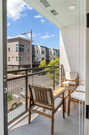 Ein Balkon mit Holztisch und -stühlen, Blick auf benachbarte Gebäude und einem klaren Himmel.