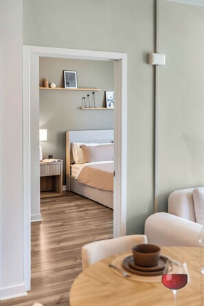 Ein modernes Hotelzimmer mit Bett, Nachttisch, Lampe und einem Essbereich mit Tisch und Weinglas.