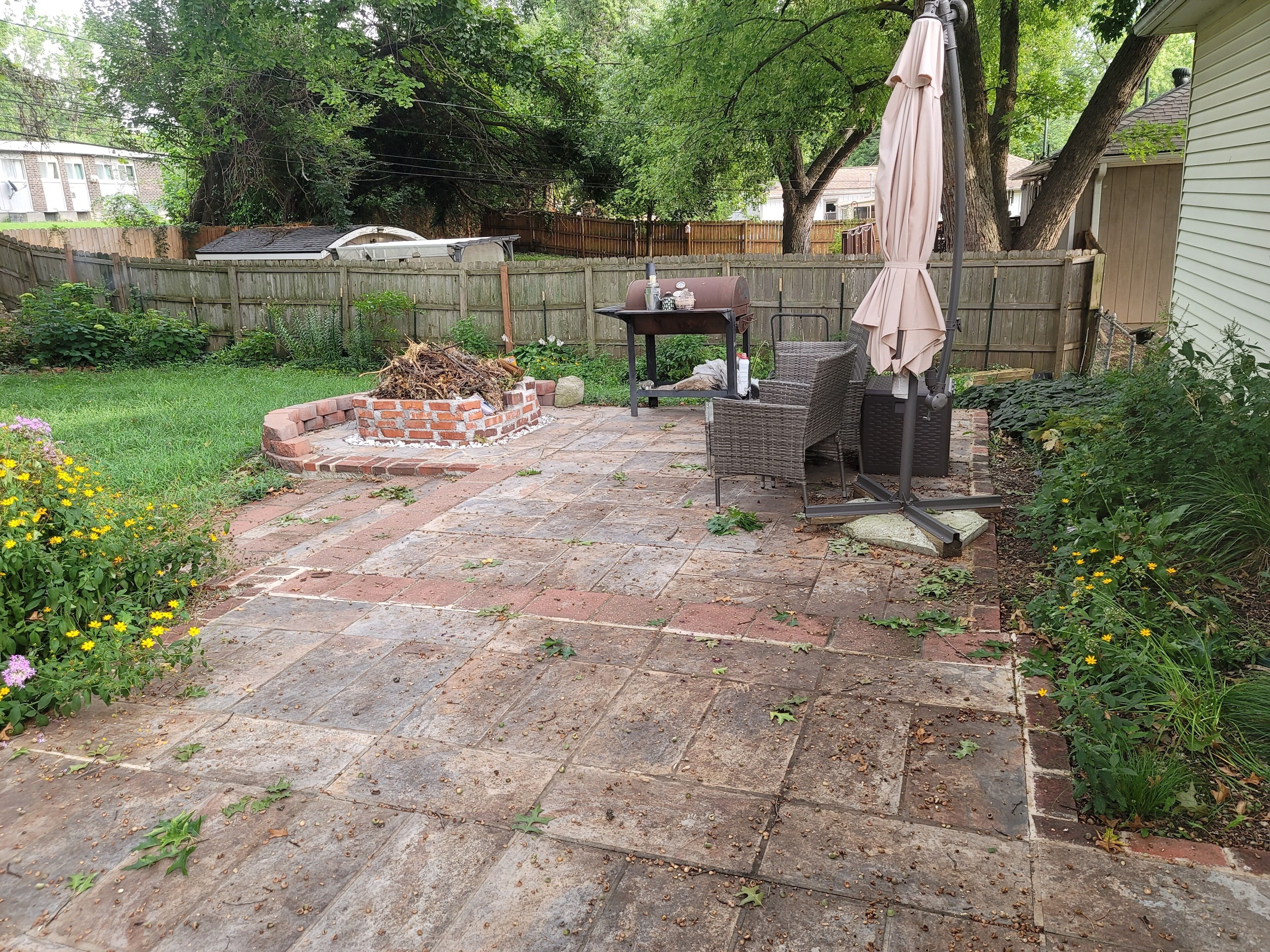 A backyard patio with a brick fire pit, outdoor furniture, and a wooden fence.