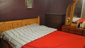 Ein Schlafzimmer mit einem hölzernen Bett, einer roten Decke, einer dunklen Kommode und einem Spiegel.