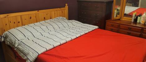 Une chambre à coucher avec un lit en bois, une couverture rouge, une commode sombre et un miroir.
