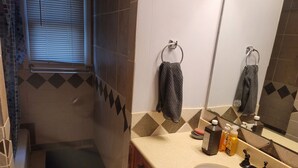 Ein Badezimmer mit Waschbecken, Spiegel, Handtuchhalter und einem Fenster mit Jalousien.