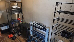 Ein Heim-Fitnessraum mit Trainingsgeräten, einem Schuhregal und einem Fernseher auf einem Standfuß.