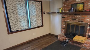 A room with a fireplace, a wooden floor, a patterned window, and a brick wall. - Charming 3-bedroom house, fenced backyard and AC in brilliant Overland Park (Overland Park)