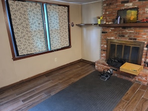 Una habitación con chimenea, suelo de madera, ventana con diseño y pared de ladrillo.