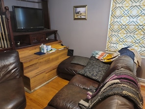 Ein Wohnzimmer mit einer Holzunterhaltungsecke, einem Ledersofa und einer gemusterten Decke.