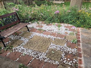 Un jardín con un banco y un área pavimentada con piedras y ladrillos.