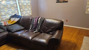 A brown leather sofa with a blanket, patterned pillows, and a wall with a giraffe painting. - Charming 3-bedroom house, fenced backyard and AC in brilliant Overland Park (Overland Park)