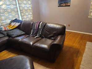 Un sofá de cuero marrón con una manta, almohadas estampadas y una pared con un cuadro de jirafa.