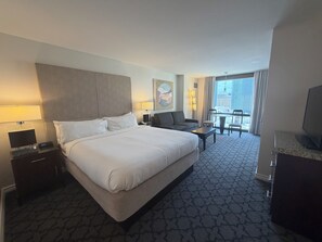 Habitación de hotel con una cama grande, un sofá, un escritorio y un balcón con vistas.