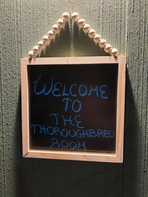A chalkboard sign with the message 'WELCOME TO THE THOROUGHBRD ROOM' mounted on a wooden wall.