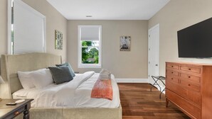 Un dormitorio con cama, cómoda, televisión y ventana con persianas.