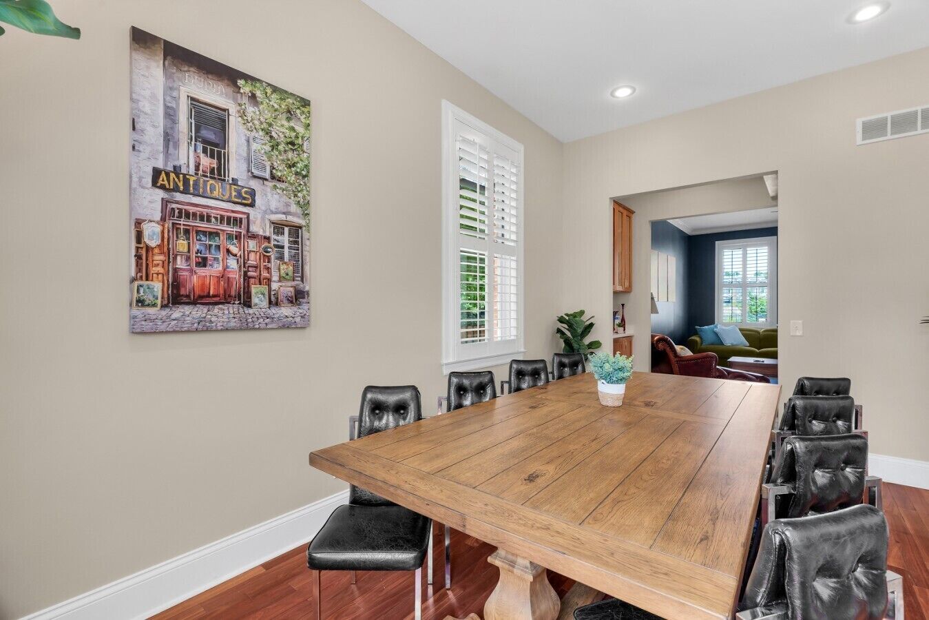 Un espace repas avec une longue table en bois, des chaises en cuir noir et un tableau accroché au mur.