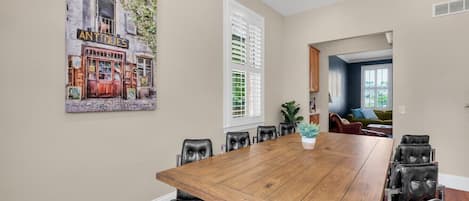 Un espace repas avec une longue table en bois, des chaises en cuir noir et un tableau accroché au mur.