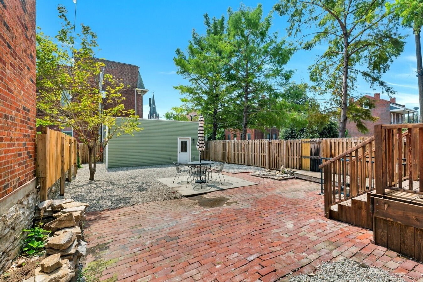 Ein Garten mit Terrasse, Holzlattenzaun und Backsteinmauer.