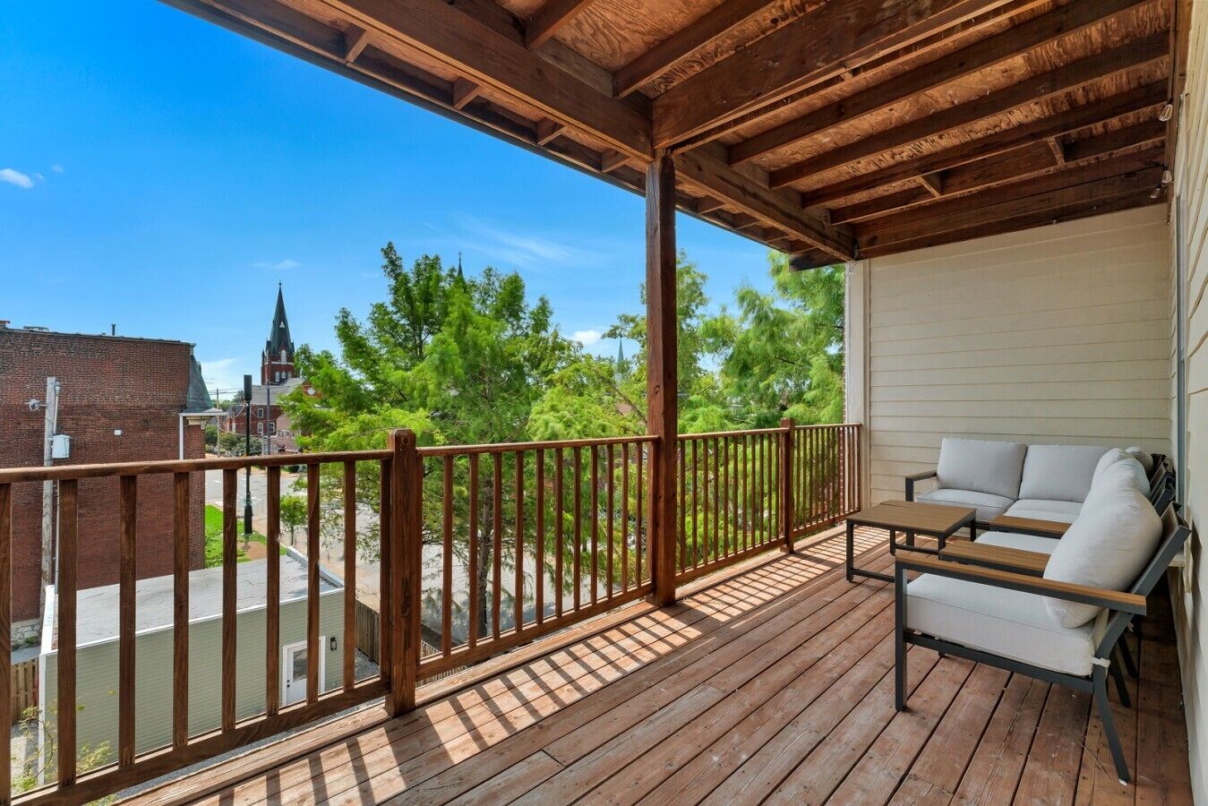 A covered outdoor deck with a wooden railing, a sofa, and a table.