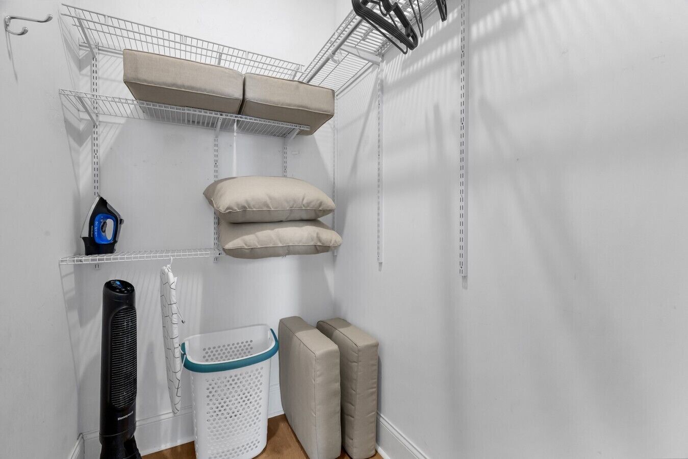 Un lavadero con un tendedero metálico, tabla de planchar, cesto de ropa y almohadones de almacenamiento.