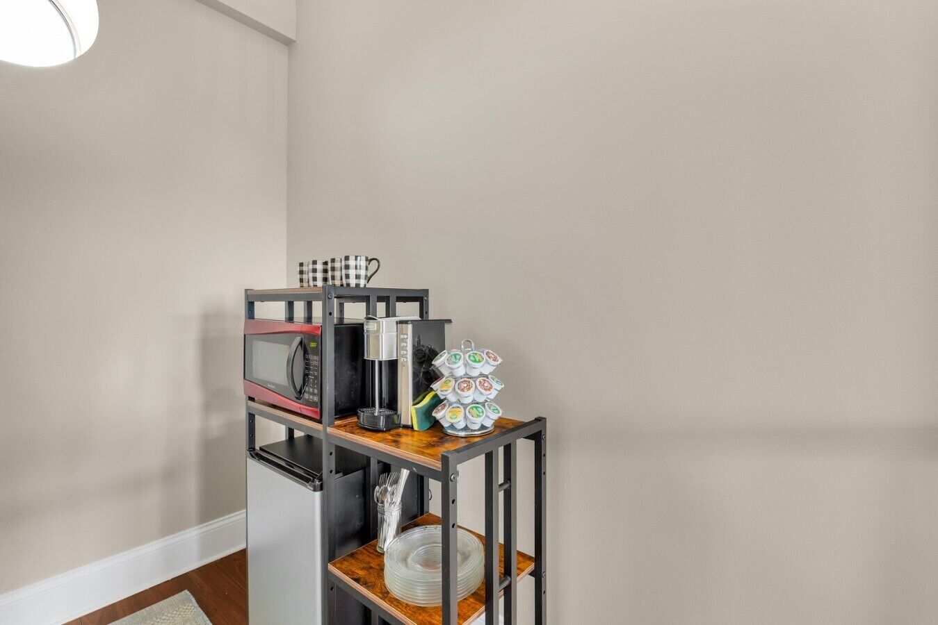 Una kitchenette con microondas, cafetera y juego de té sobre una estantería metálica.