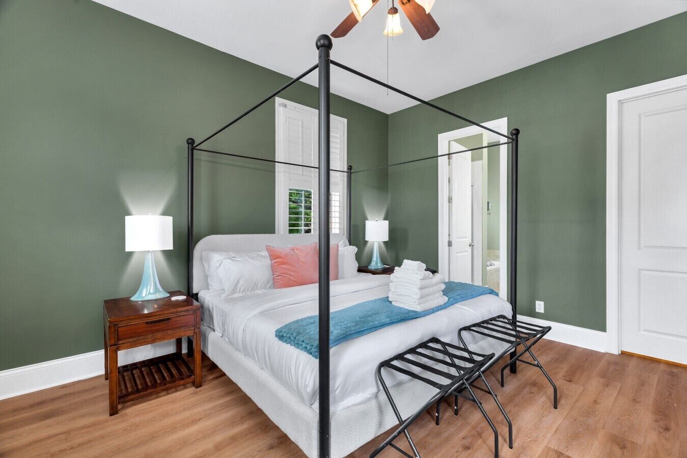 A four-poster bed with a wooden floor, two bedside tables with lamps, and a ceiling fan.