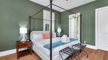 A four-poster bed with a wooden floor, two bedside tables with lamps, and a ceiling fan.