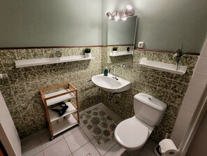A bathroom with a toilet, sink, and mirror. There are shelves above the sink and a small shelf above the mirror. - "Am Binnenwasser" Vacation Rental: Apartment with an alcove bedroom, kitchen, and large sunroom (Neustadt in Holstein)