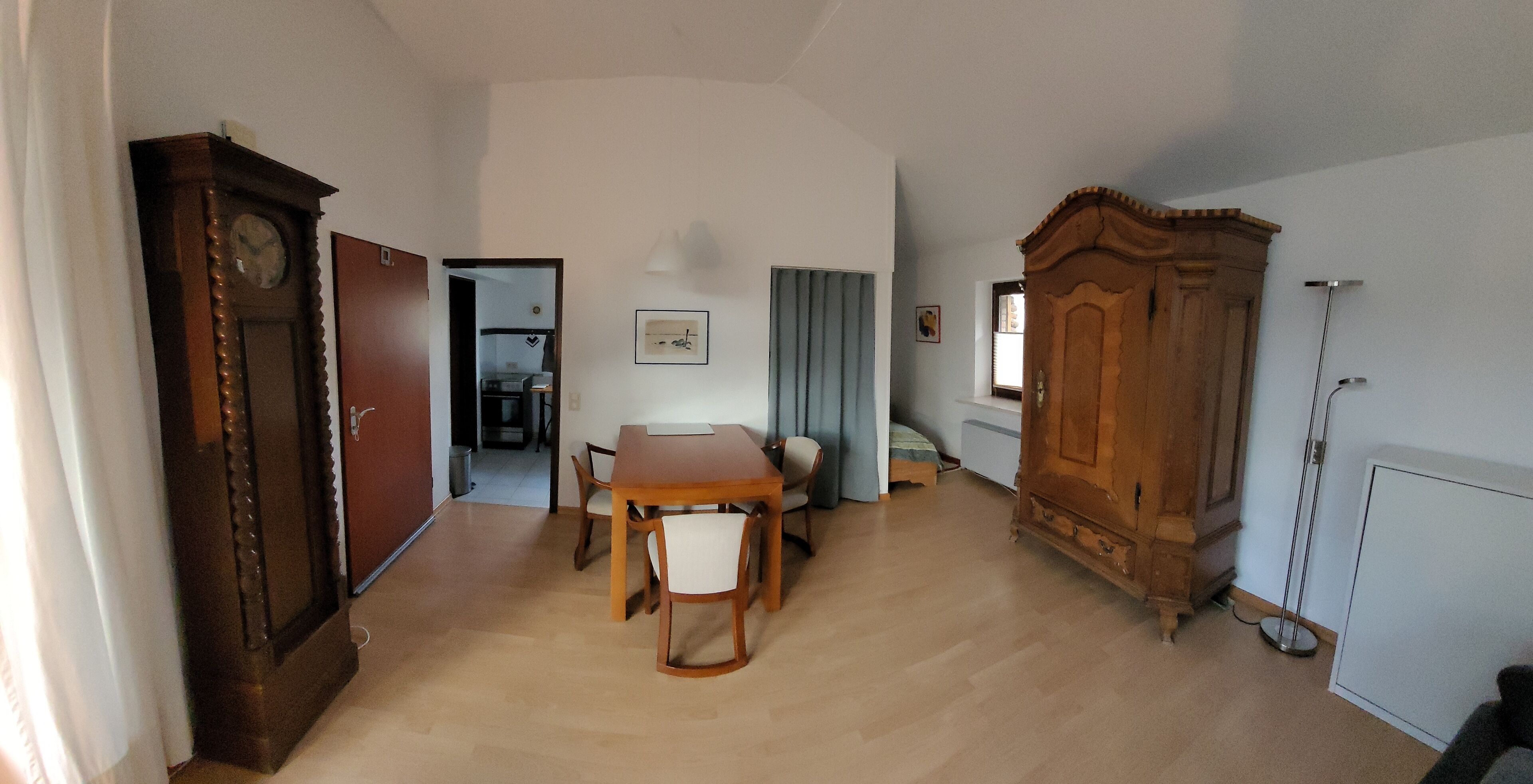 Une pièce comprenant une table à manger en bois, des chaises, une grande armoire en bois, un lit et un radiateur.