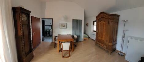 Une pièce comprenant une table à manger en bois, des chaises, une grande armoire en bois, un lit et un radiateur.