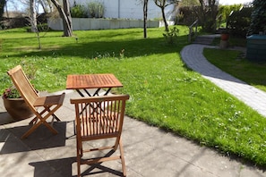 A patio with two wooden chairs and a table, surrounded by a well-maintained lawn and a paved walkway. - "Am Binnenwasser" Vacation Rental: Apartment with an alcove bedroom, kitchen, and large sunroom (Neustadt in Holstein)