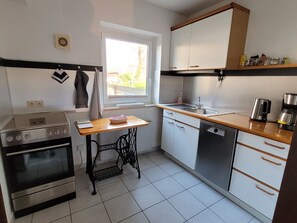 A compact kitchen with a stove, sink, and dishwasher, featuring a window and a small table. - "Am Binnenwasser" Vacation Rental: Apartment with an alcove bedroom, kitchen, and large sunroom (Neustadt in Holstein)