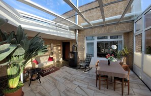 A covered patio area with a brick wall, a glass door leading outside, a table with chairs, a sofa, and a large potted plant. - "Am Binnenwasser" Vacation Rental: Apartment with an alcove bedroom, kitchen, and large sunroom (Neustadt in Holstein)