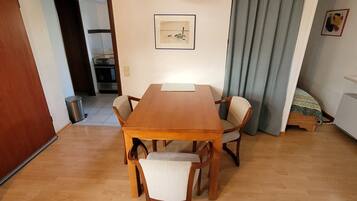 Ein Essbereich mit einem Holztisch und Stühlen, eine Küche im Hintergrund und ein Bett mit einem gemusterten Überwurf.