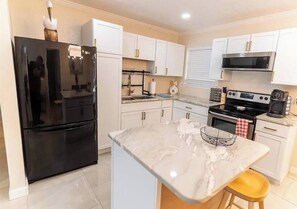 A modern kitchen with white cabinets, a black refrigerator, a stove, and a marble countertop. - Gulf Breeze- 10 min to beaches, 4bed, 2.5bath (Gulf Breeze)