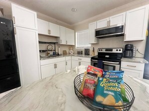 Une cuisine avec des meubles blancs, un réfrigérateur noir, une cuisinière et une machine à café.