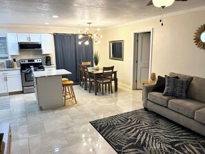 A modern kitchen with a central island, dining area with chairs, a sofa, and a patterned rug. - Gulf Breeze- 10 min to beaches, 4bed, 2.5bath (Gulf Breeze)