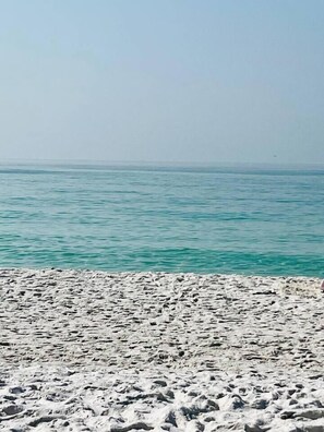 Ein Strand mit sandigem Vordergrund und ruhigem Wasser im Hintergrund.