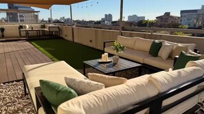 Eine Dachterrasse mit einer Sofagarnitur, einem kleinen Tisch mit einer Pflanze und Blick auf die Stadt.