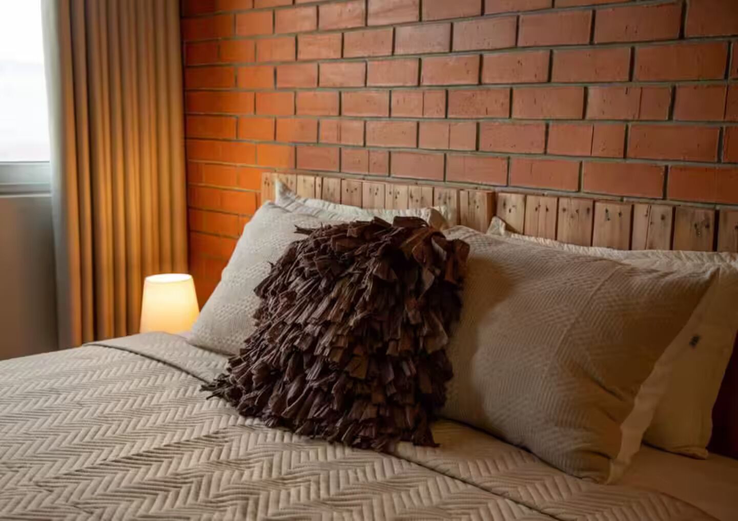 Ein Hotelzimmer mit Backsteinwand, einem Bett mit gemusterten Betttextilien und einer Lampe daneben.