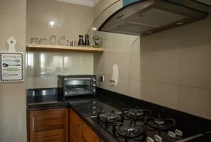 Una cocina con horno tostador empotrado, estufa a gas y un estante con utensilios de cocina.