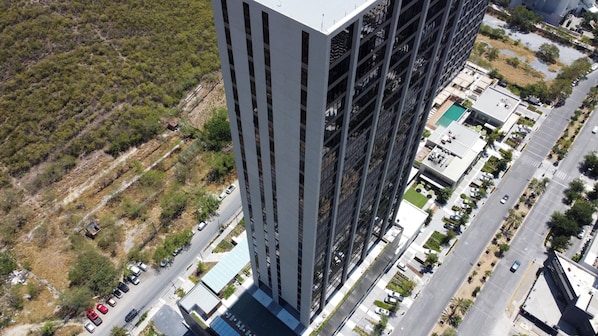 A high-rise building with a modern architectural design, featuring a prominent vertical facade and a rooftop pool area. - Olma (San Pedro Garza García)