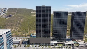 Un edifici modern i alt, amb façana de reixa, envoltat d'una zona enjardinada amb palmeres i un aparcament.