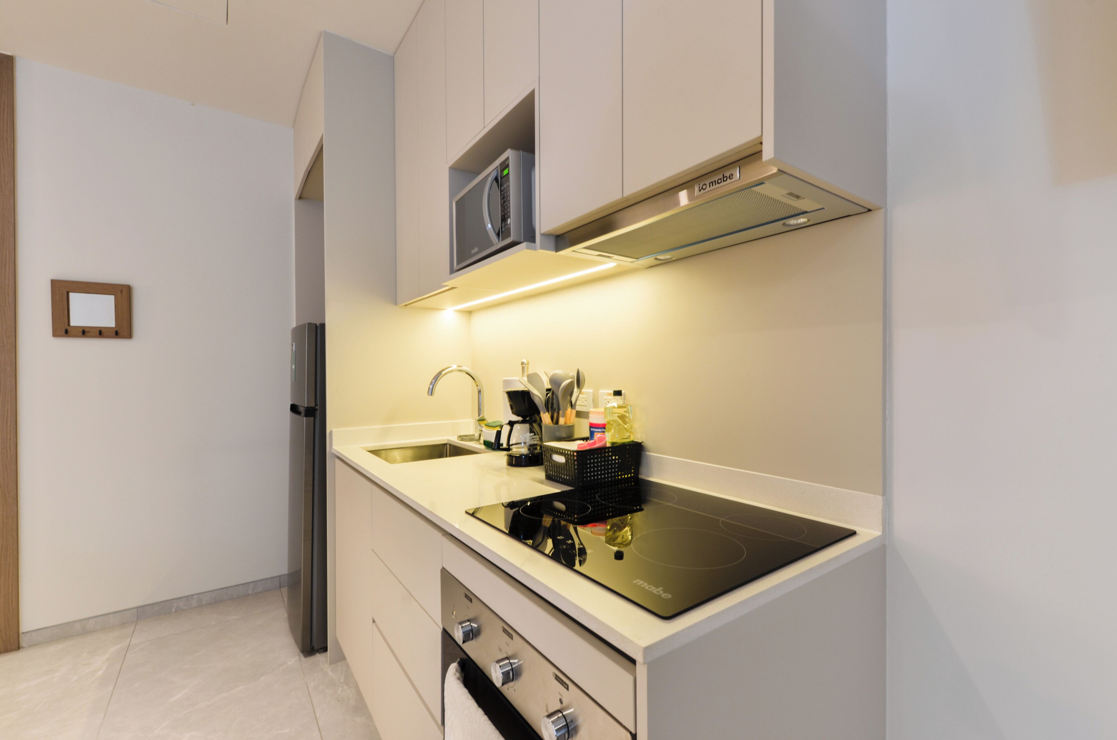 A modern kitchen with a built-in microwave, a stainless steel refrigerator, and a black induction cooktop.