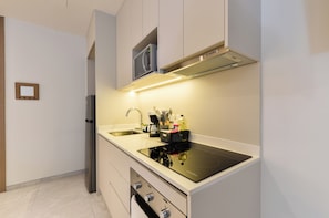 A modern kitchen with a built-in microwave, a stainless steel refrigerator, and a black induction cooktop. - Olma (San Pedro Garza García)