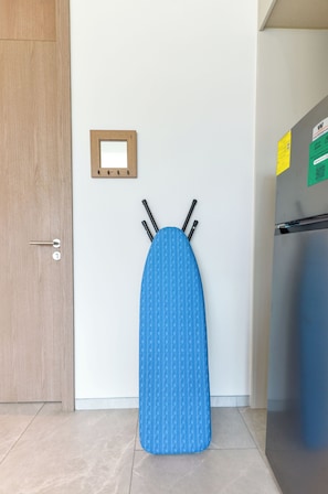 A room with a wooden door, a wall-mounted light switch, and a blue ironing board with four pegs. - Olma (San Pedro Garza García)