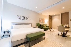 A modern hotel room with a large bed, a green sofa, a small table, and a desk with chairs. - Olma (San Pedro Garza García)