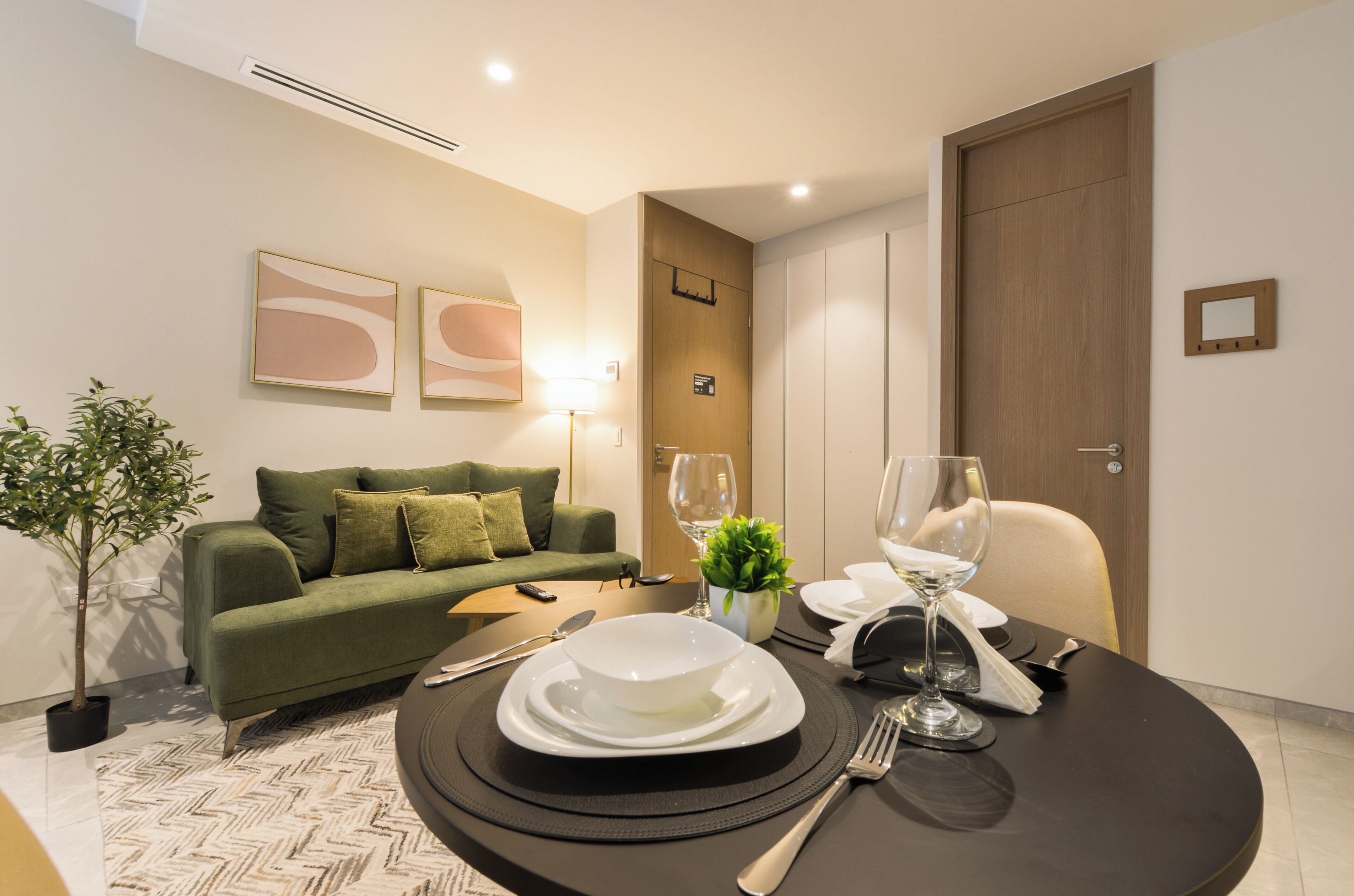 Un comedor con una mesa redonda lista para dos personas, un sofá verde y arte abstracto en la pared.