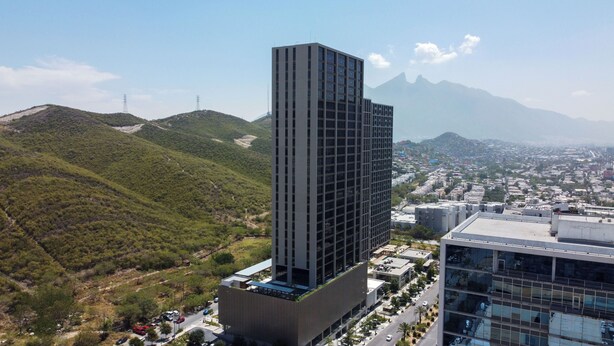 Un edifici modern i alt, amb teulada plana i façana de vidre, envoltat d'un paisatge ondulat i un skyline urbà al fons.