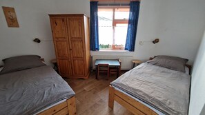 A room with two wooden beds, a wooden wardrobe, a small table, and a window with curtains. - Cozy bungalow near the beach (Julianadorp)
