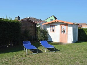 Ein kleines Haus mit Gartenhaus, zwei blauen Liegestühlen und einem gepflegten Rasen.