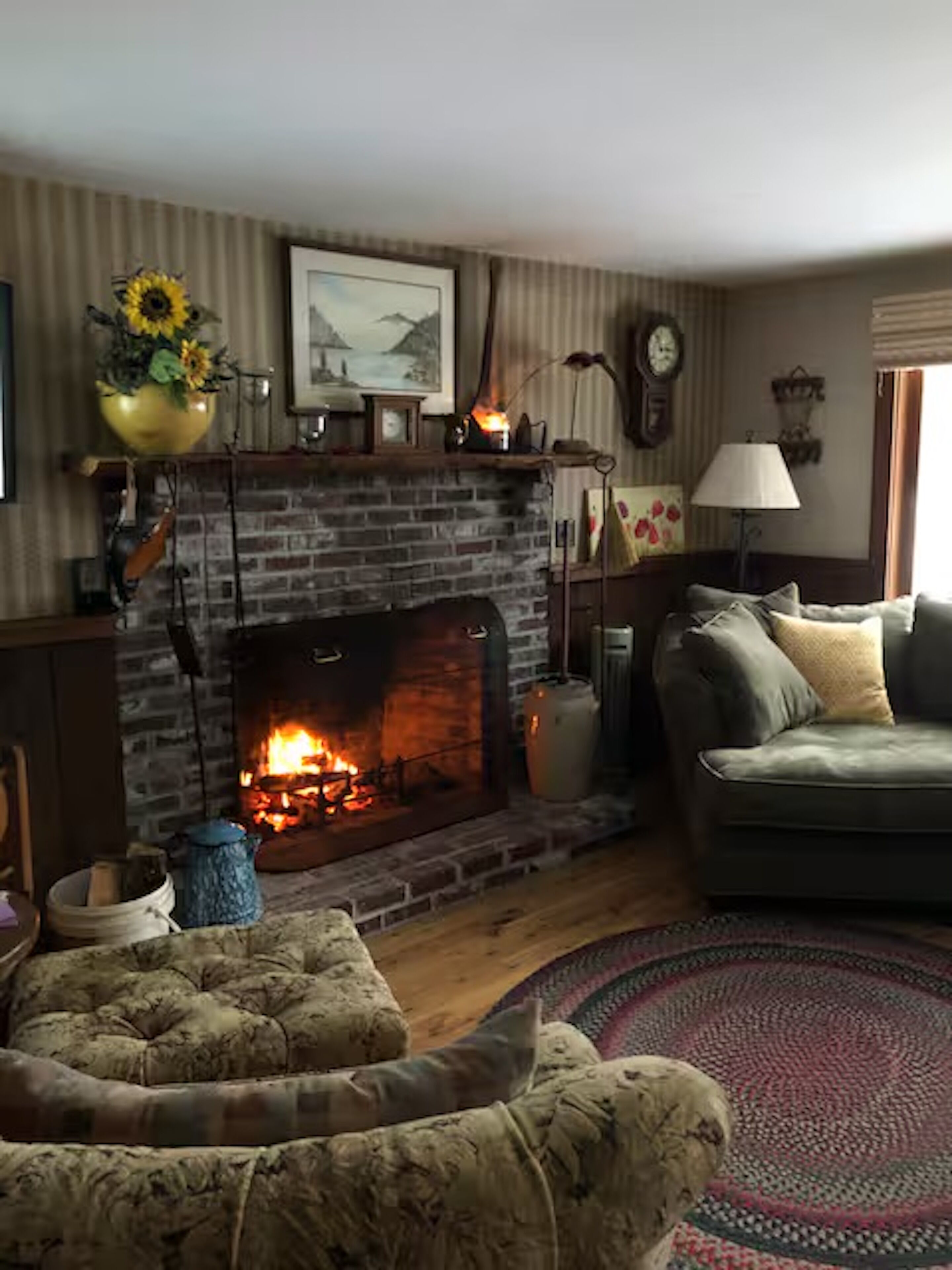 A living room with a brick fireplace, a sofa, a patterned rug, and a wall-mounted lamp.