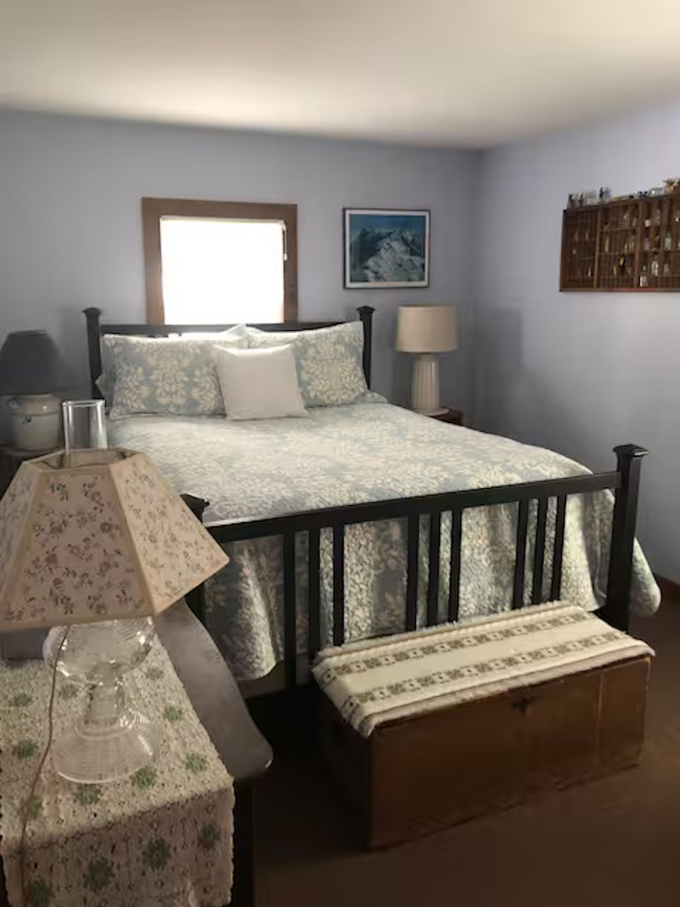 A bedroom with a bed, bedside tables, a lamp, a wooden bench, and a wall-mounted shelf.